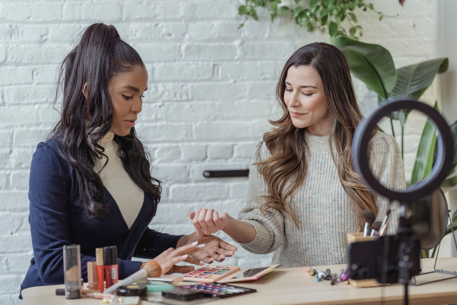 Jovens blogueiras multiétnicas testam maquiagem à mesa e gravam vlog com celular no tripé e ring light