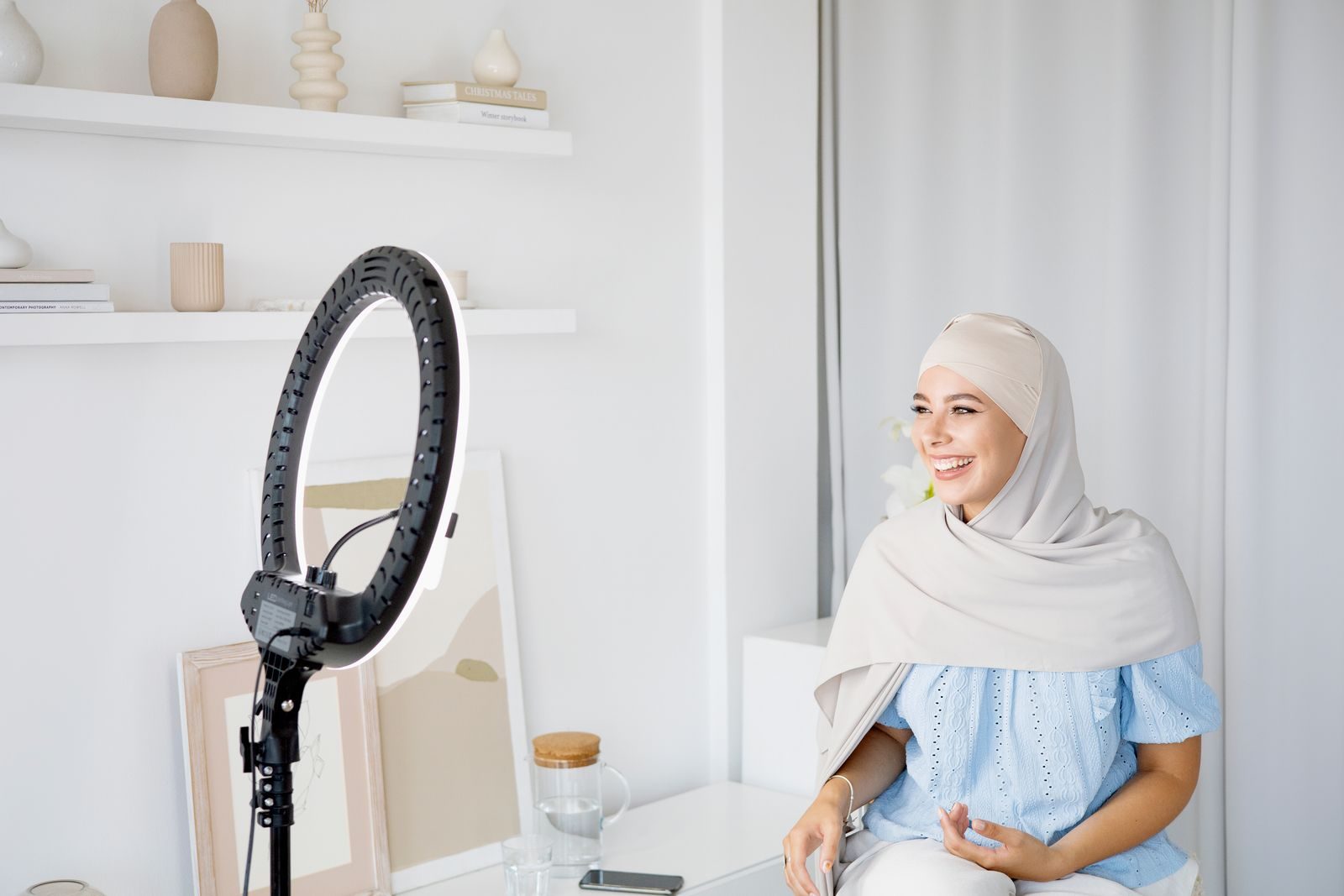 Mulher muçulmana sorridente de hijab gravando vlog em casa com ring light