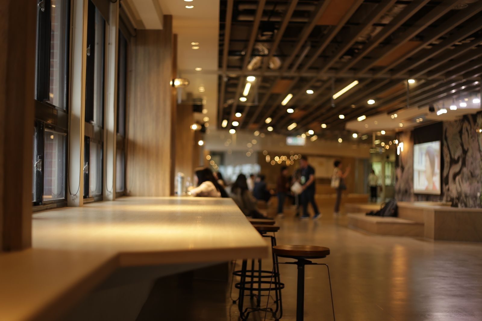 Café interno moderno com design em madeira e pessoas socializando ao fundo