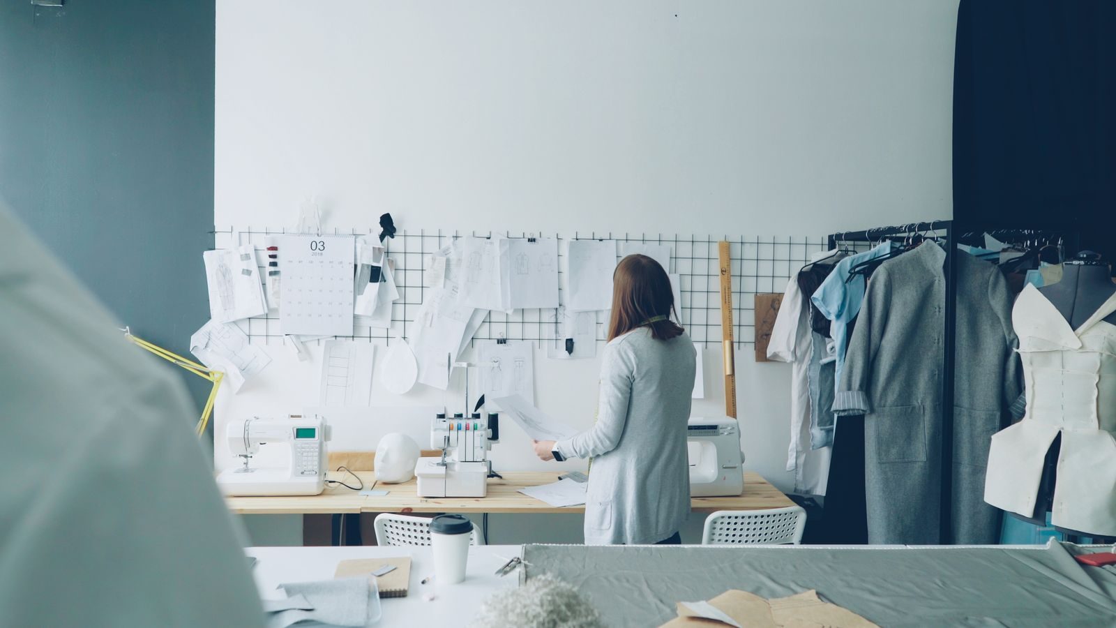 Estilista trabalhando em um ateliê moderno com máquinas de costura e criações de roupas