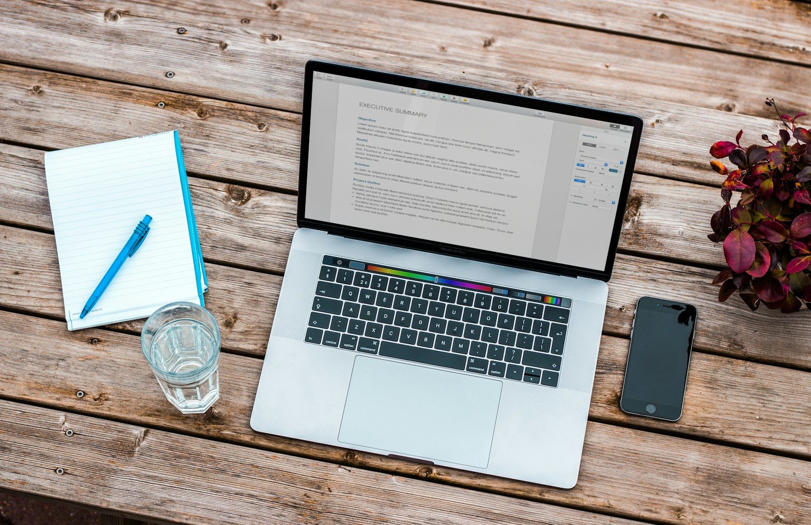 MacBook prateado ao lado de iPhone 6 cinza-espacial e copo transparente sobre madeira marrom