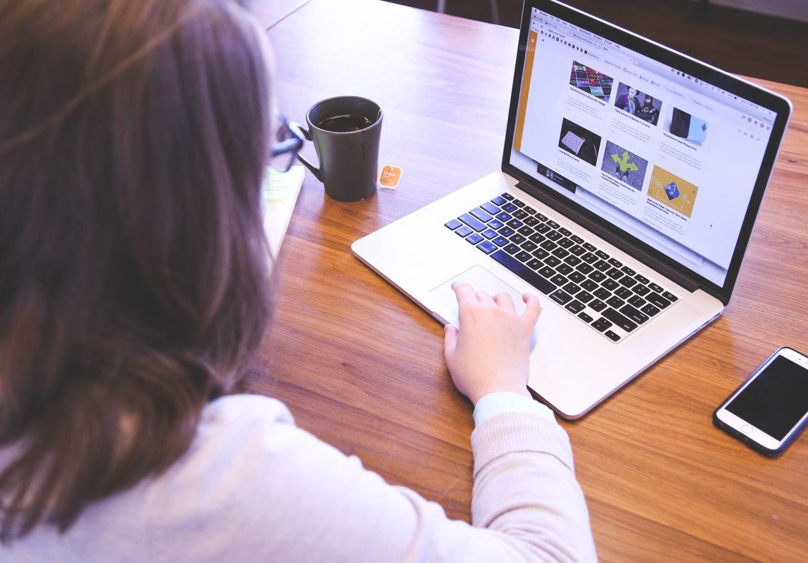Pessoa navegando na web em um MacBook em mesa de madeira com um smartphone
