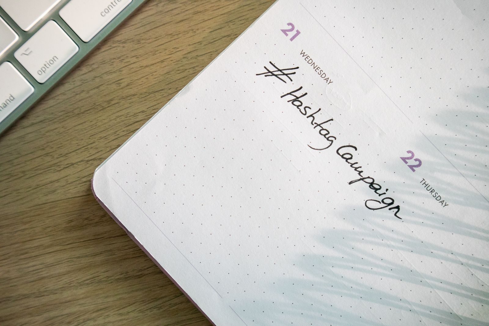 Agenda aberta com "Hashtag Campaign" escrito à mão ao lado de um teclado