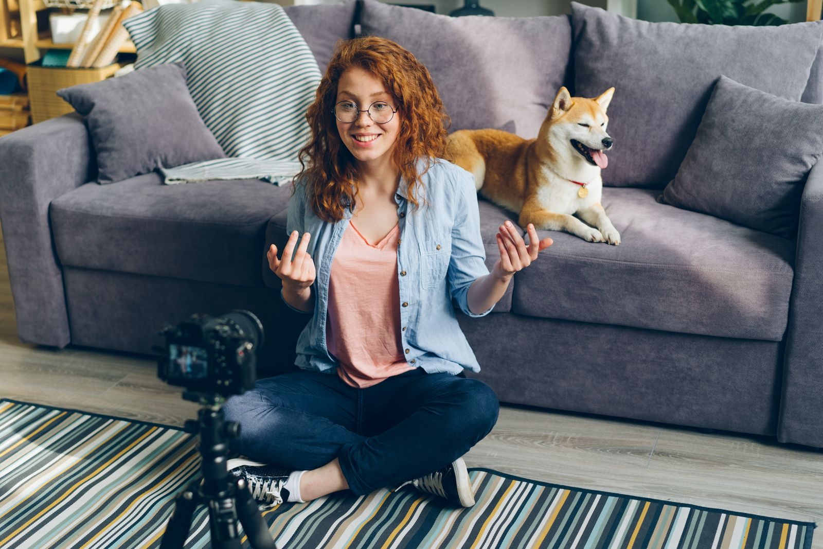 Mulher ruiva gravando vídeo em casa com seu cachorro shiba inu no sofá