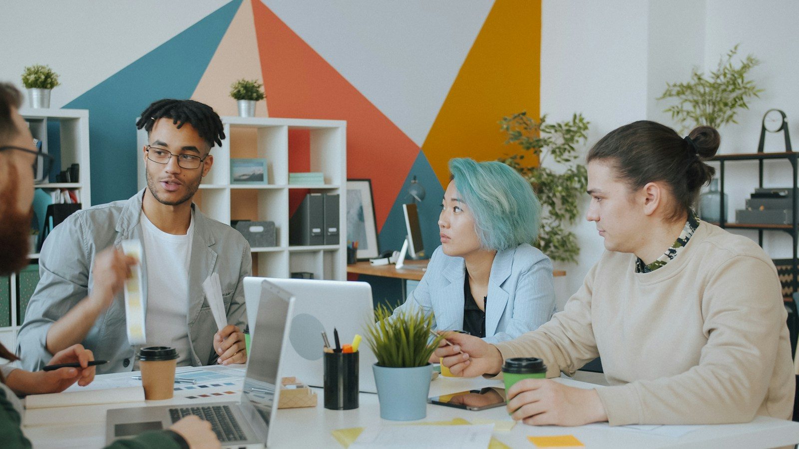 Grupo diverso de quatro pessoas colaborando em espaço de trabalho moderno e colorido